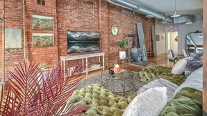 A modern living room with a brick wall, a large flat-screen TV, a white console table, and a green sofa. - Loft 40- Game Room- Sleeps 18 (Cleveland)