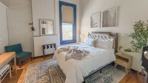 A bedroom with a bed, a chair, a desk, a window with blinds, and a plant. - Loft 40- Game Room- Sleeps 18 (Cleveland)
