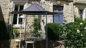 A stone building with multiple windows and a covered patio area with metal furniture. - THE LARGE COTTAGE AT CHÂTEAU SAINTE MARIE NEAR THE MARAIS POITEVIN (Fors)