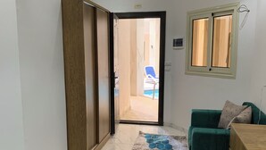 Quarto com cama, sofá verde, armário de madeira e vista para uma piscina ao ar livre.