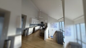 A modern kitchen with a central island, wooden flooring, and a view of the living area.