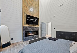 Ein modernes Schlafzimmer mit Kamin aus Stein, einem Bett mit gesteppter Bettdecke und einem an der Wand montierten Fernseher.