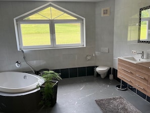Une salle de bain avec une baignoire sur pieds, des toilettes, un lavabo et une fenĂȘtre donnant sur un champ verdoyant.