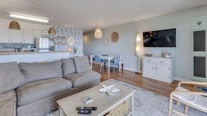 A modern living room with a sofa, coffee table, and a TV mounted on the wall. - Winds V D1 - Oceanfront Pet Friendly Condo with Pool and Close to Boardwalk (Carolina Beach)