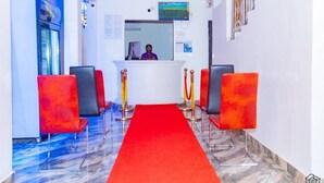 A hotel reception area with a red carpet, a reception desk, and two red chairs. - Elu Hotel Diamant (Douala)