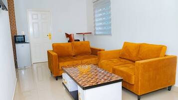 Una sala de estar con dos sofás anaranjados, una mesa de centro, un armario blanco y un microondas.