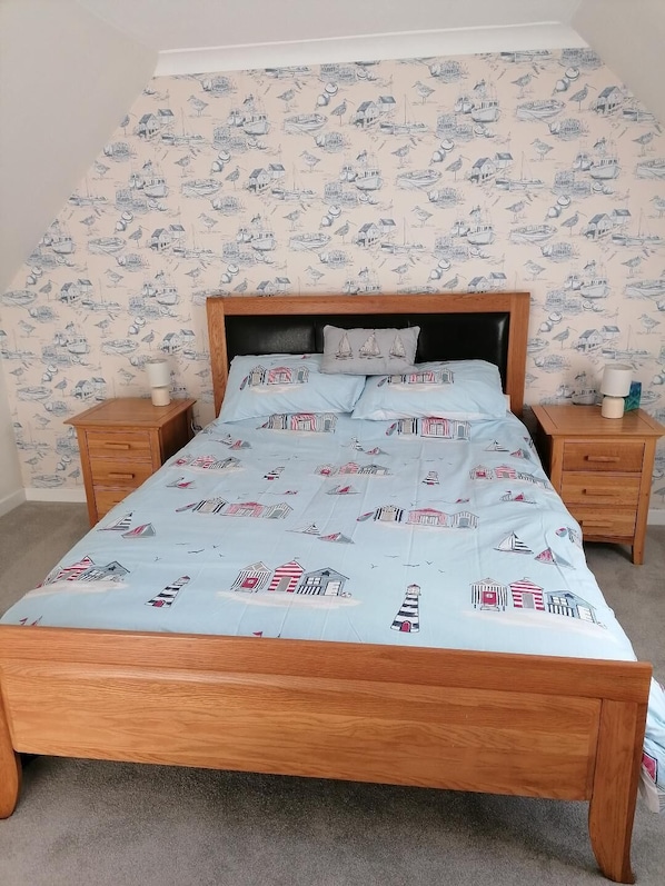 A bedroom with a wooden bed, matching nightstands, and a patterned wallpaper depicting maritime scenes.