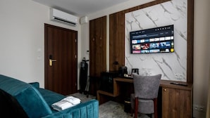 A room with a teal sofa, a wooden desk, a grey chair, and a TV mounted on a marble wall. - Sleep&Fly Okecie (Warsaw)
