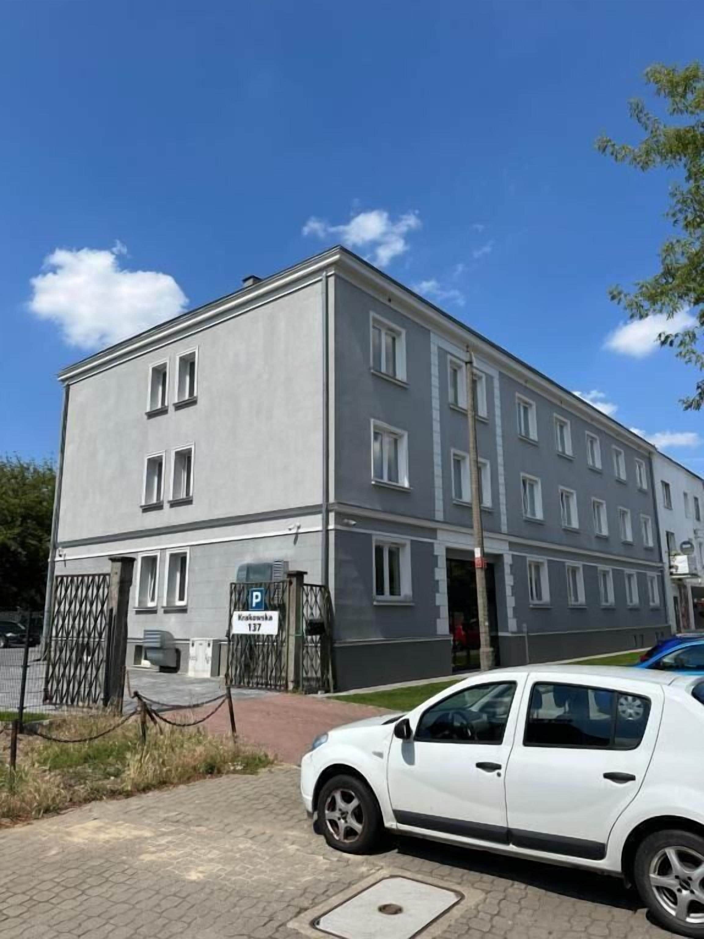 Ein mehrstöckiges Gebäude mit grauer Fassade, einem verschlossenen Eingang und einem weißen Auto davor.