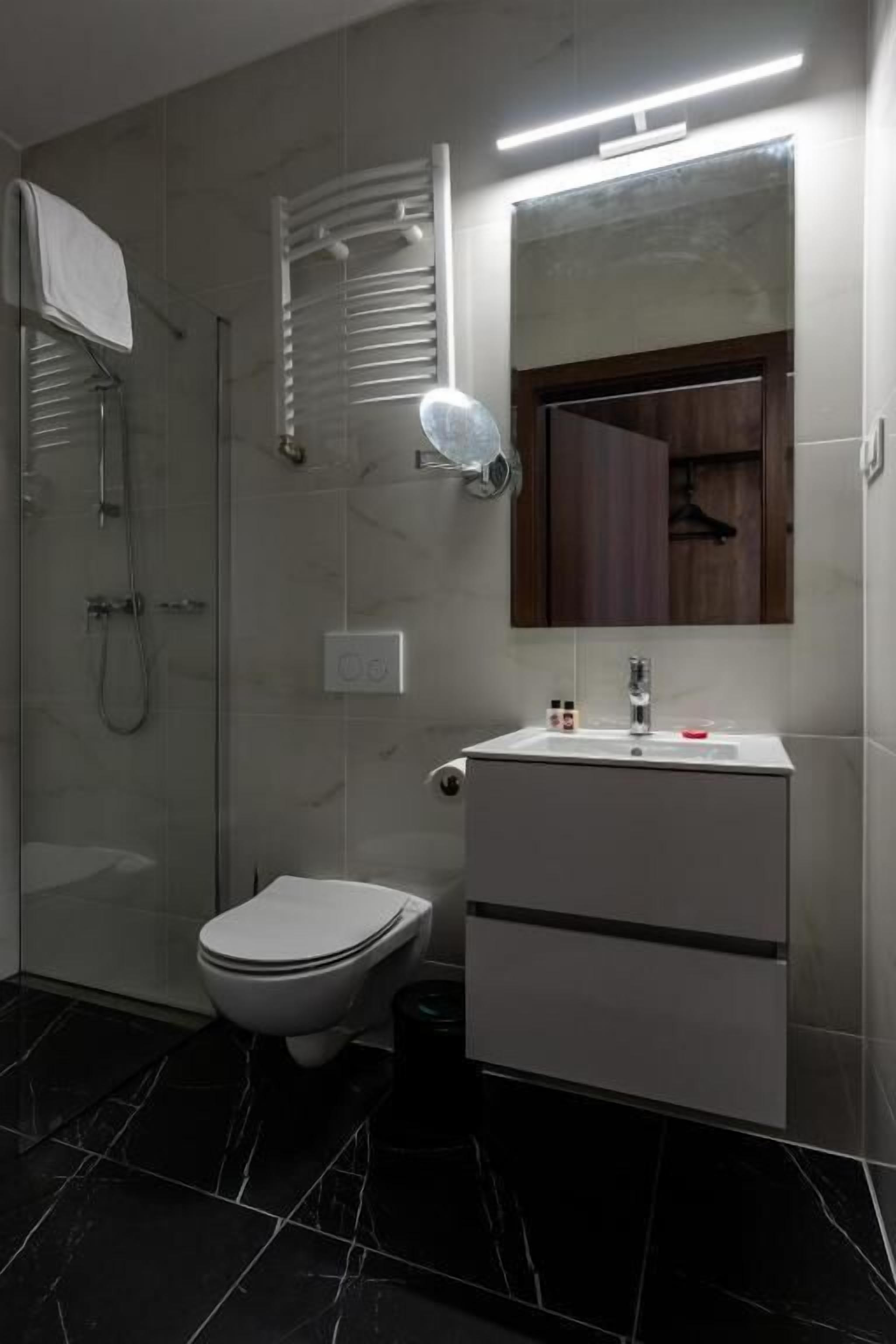 Une salle de bain moderne avec une douche à parois de verre, des toilettes blanches et un meuble-lavabo avec un miroir.