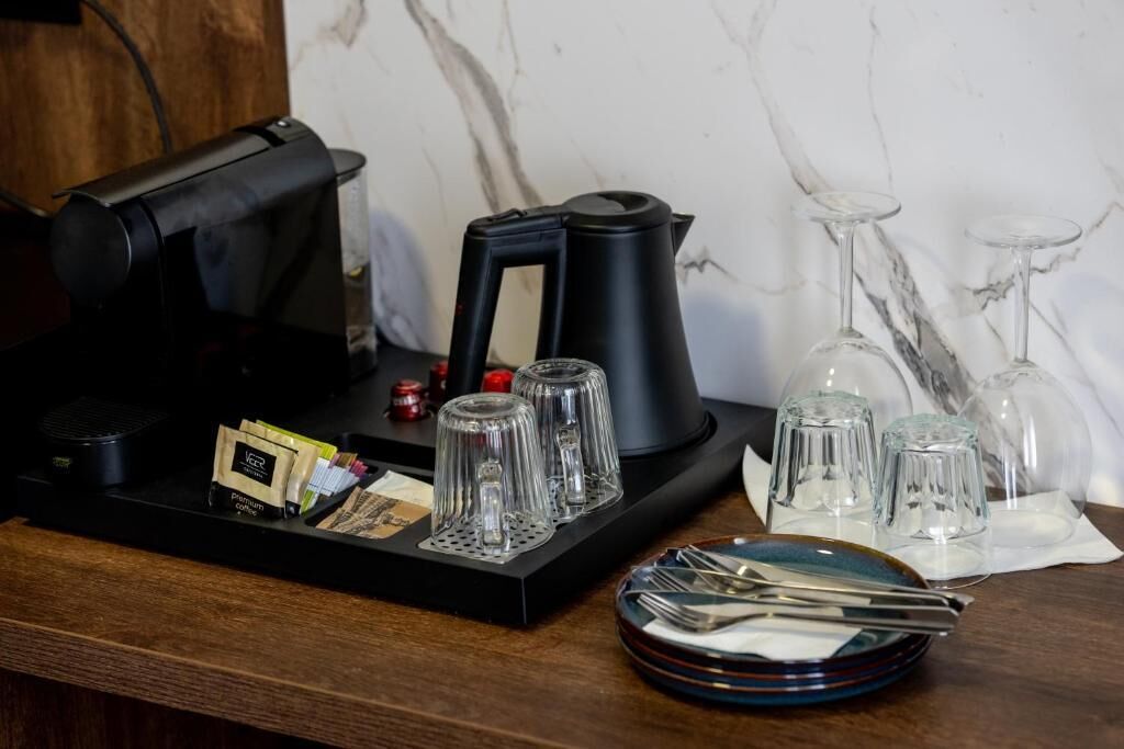 A coffee station with a coffee machine, a kettle, and a tray with coffee pods and glasses.