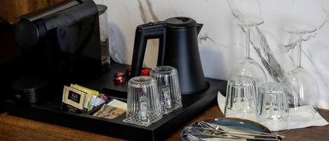 Una estación de café con una cafetera, un hervidor y una bandeja con cápsulas de café y vasos.