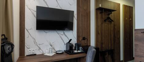 Habitación de hotel moderna con pared de mármol, paneles de madera, televisor de pantalla plana, escritorio con cafetera y una silla.