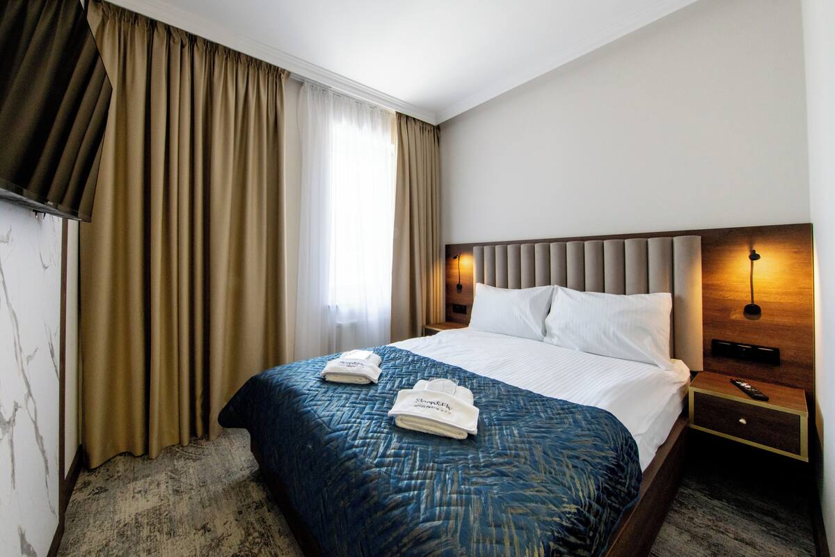 Una habitación de hotel con una cama grande, una mesita de noche con un control remoto y una lámpara de pared.