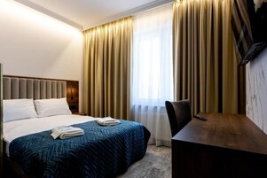 A hotel room with a bed, a desk, and a TV.