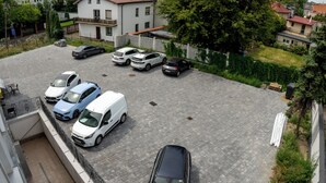 A parking area with several cars, a white building with a balcony, and a tree in the background. - Sleep&Fly Okecie (Warsaw)