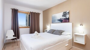 Ett modernt hotellrum med en stor säng, en stol, ett nattduksbord och en tavla på väggen.