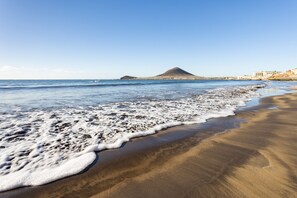 Ein Strand mit einem Berg im Hintergrund und blauem Himmel.