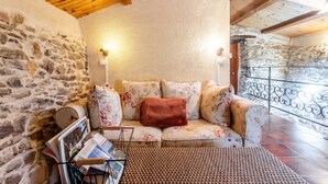 A cozy room with stone walls, a wooden ceiling, a cushioned sofa with floral upholstery, and a woven floor mat.