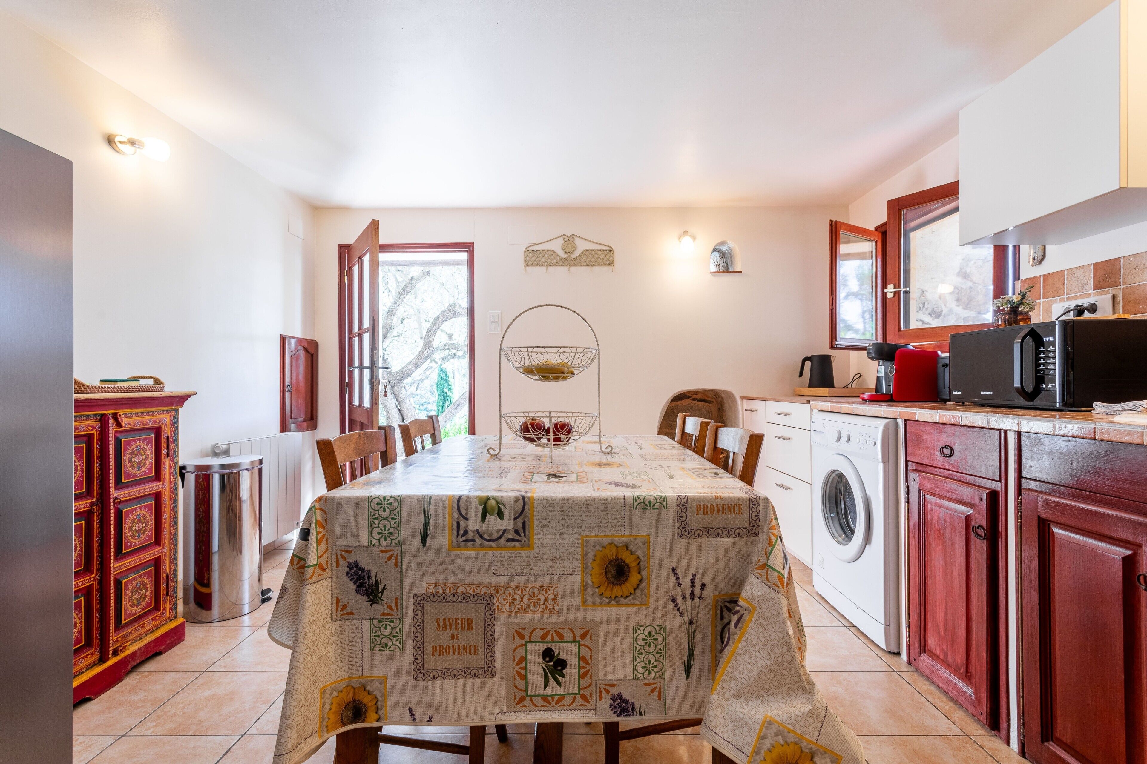 Un comedor con una mesa preparada para cuatro personas, una lavadora, un microondas y un armario con puerta roja.