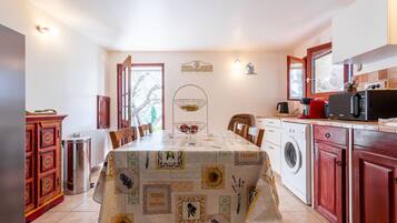 Een eethoek met een tafel gedekt voor vier personen, een wasmachine, een magnetron en een kast met een rode deur.