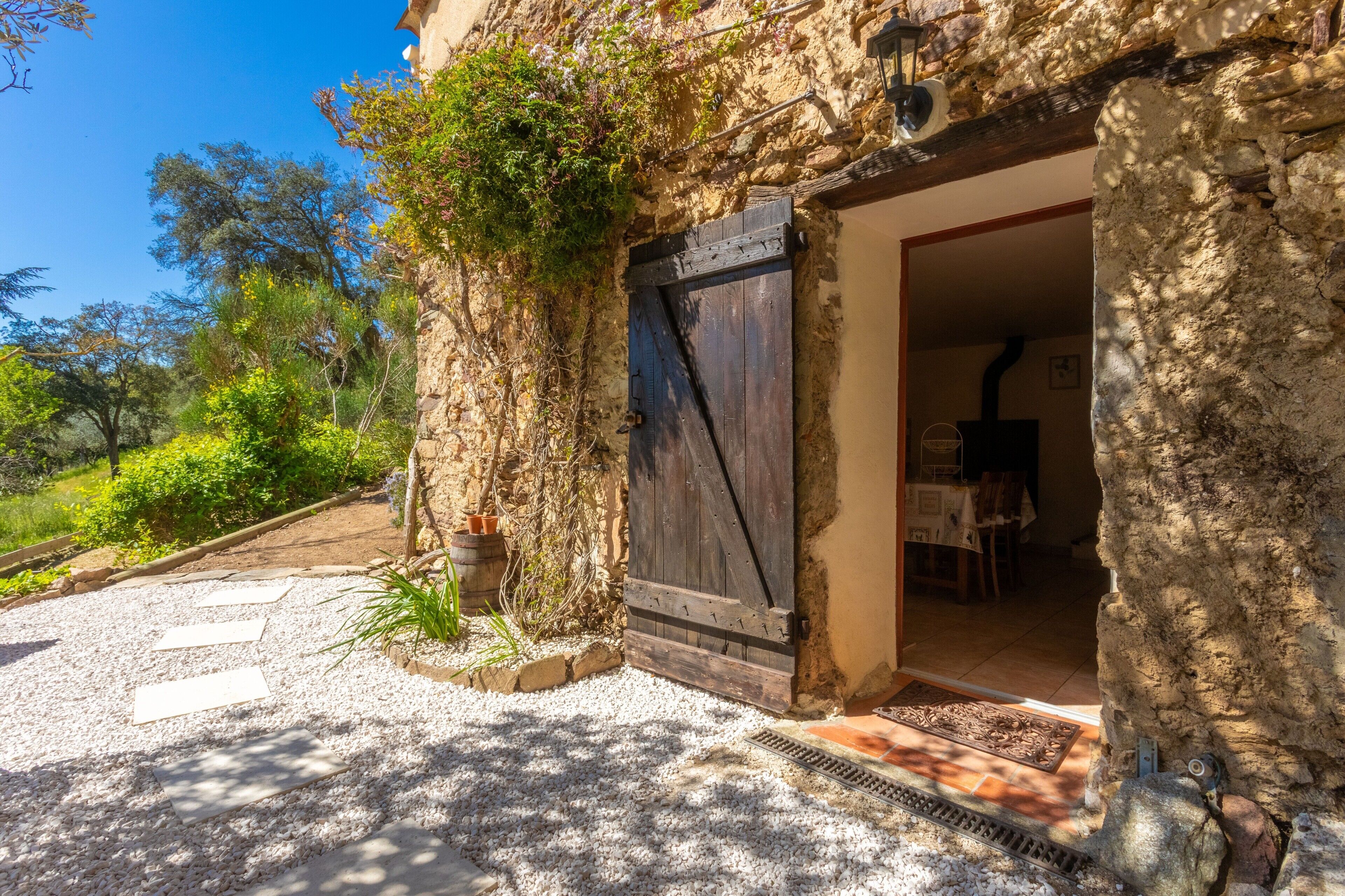 A rustic stone building with a wooden door, a gravel pathway, and a garden area.
