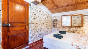 A room with a wooden door, stone walls, a bed with a white bedspread, and a mirror on the wall.