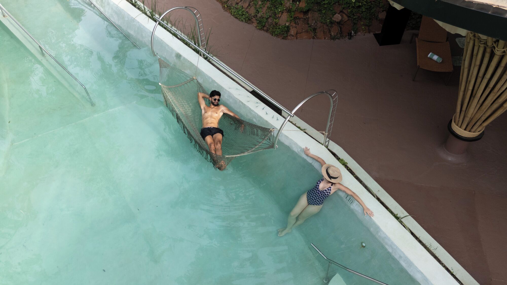 Una piscina con una persona en una hamaca y otra nadando.