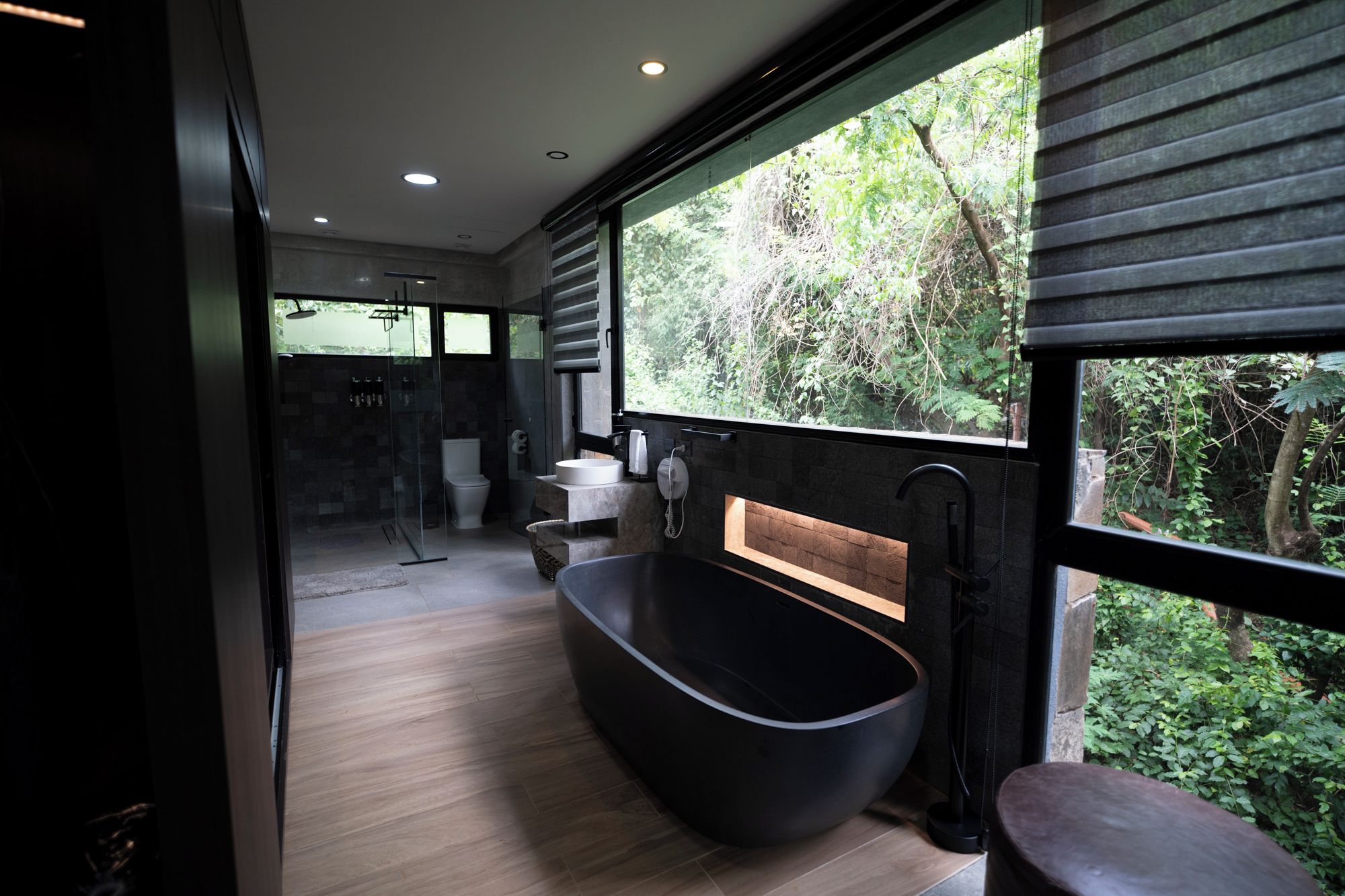 Un baño moderno con una bañera independiente, una cabina de ducha de vidrio y vistas a un jardín exuberante.