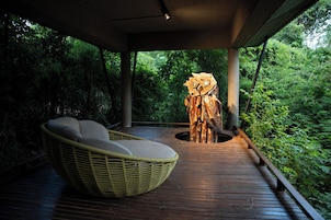 Een houten terras met een rieten stoel en een houten sculptuur.