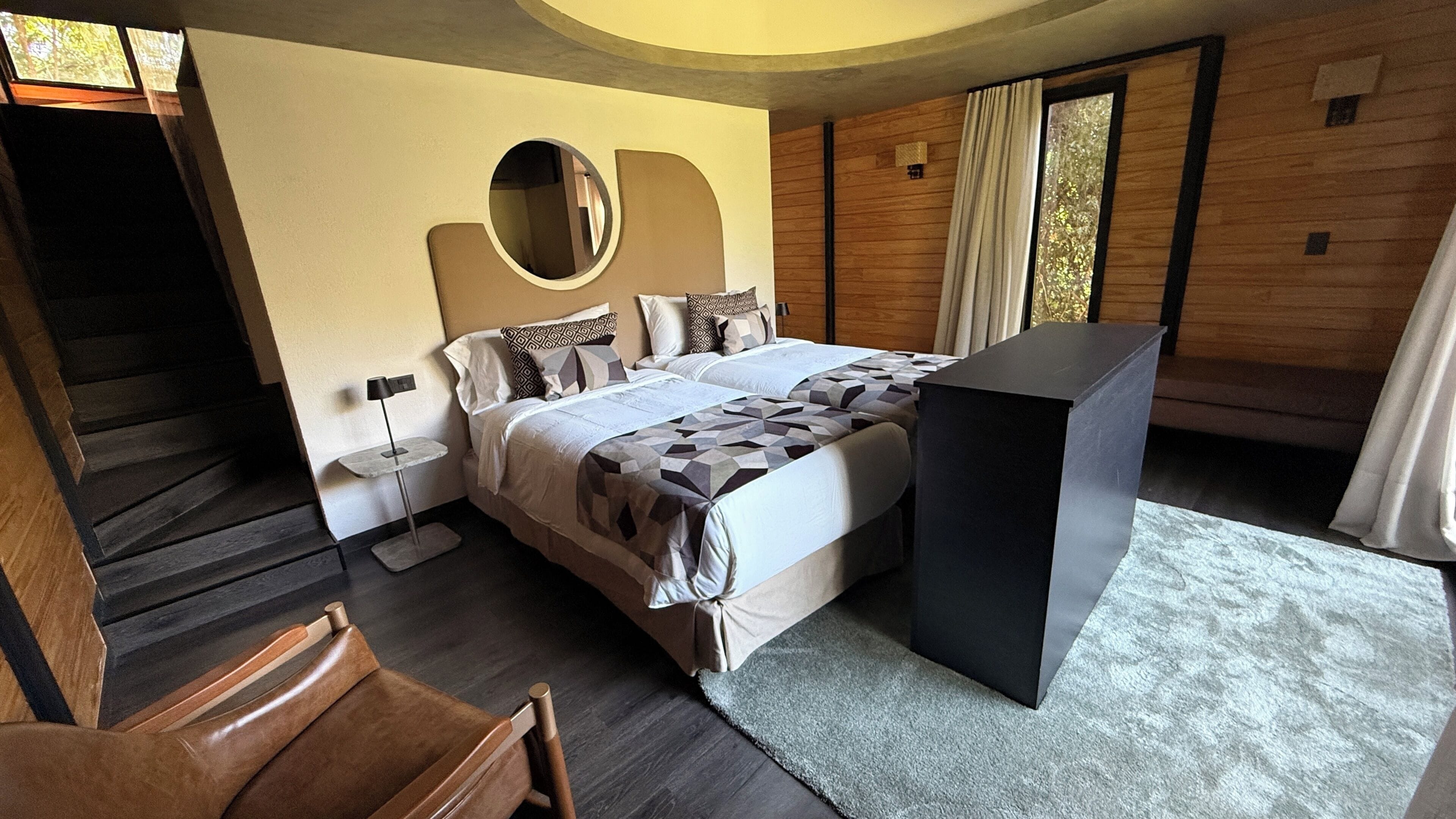 Un dormitorio con cama, escritorio, silla, espejo redondo y una escalera.