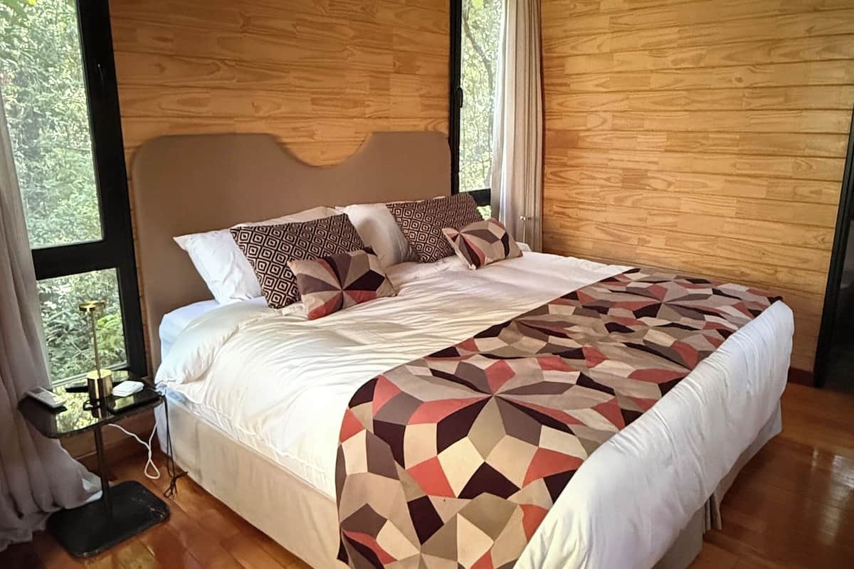 Un dormitorio espacioso con una cama grande, suelo de madera y vistas a la vegetación por la ventana.