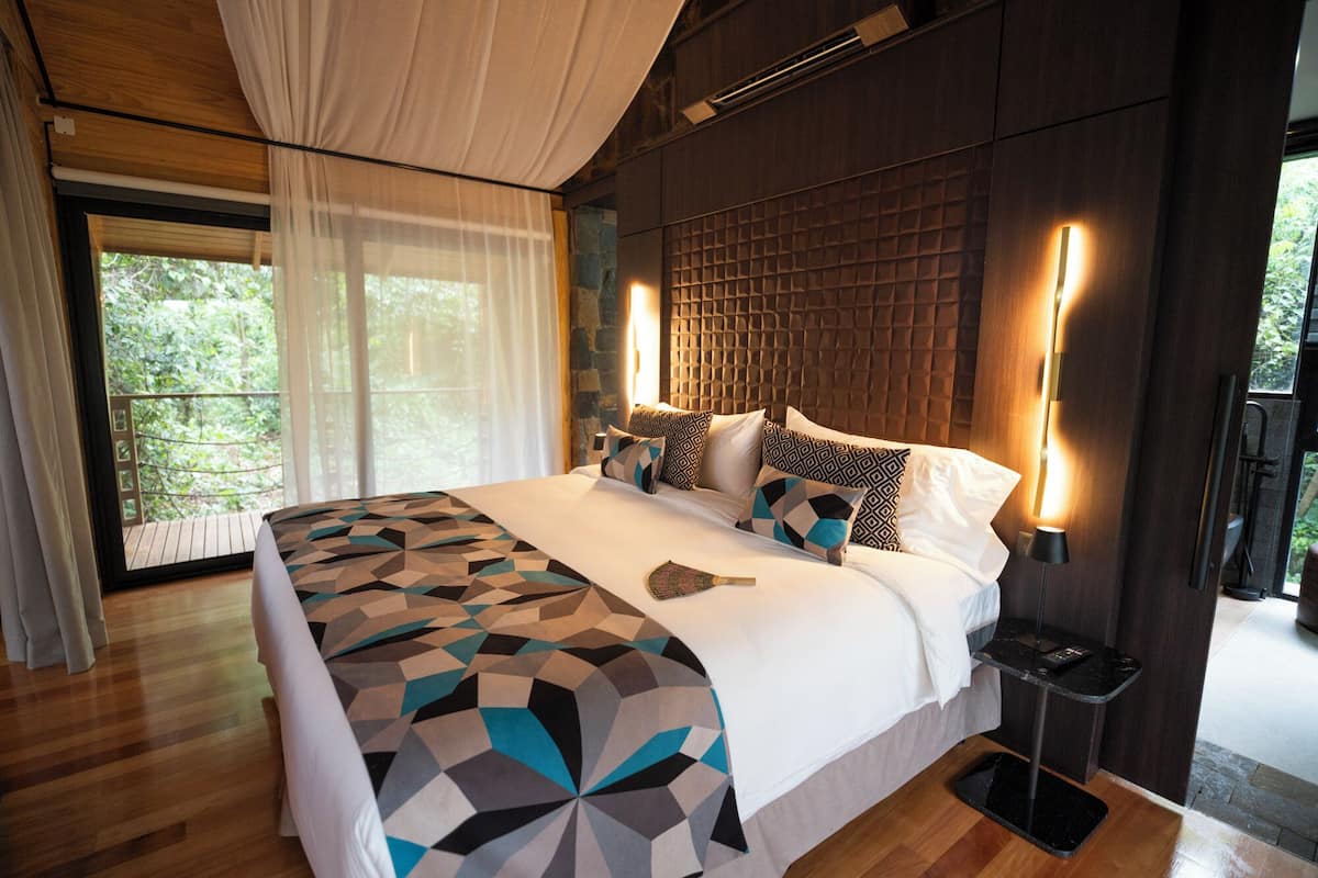 Un dormitorio moderno con una cama grande, ropa de cama estampada con motivos geométricos, un cabecero de madera y vistas a zonas verdes.