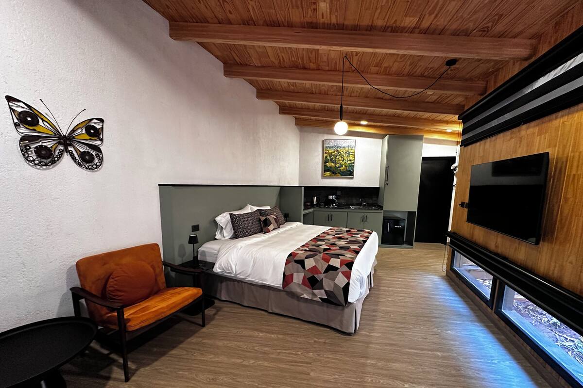 Un dormitorio con cama, mesita de noche, una silla, televisor y techo de madera.