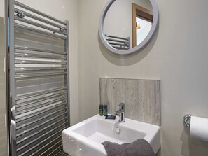 Een badkamer met een glazen douchecabine, een wit wastafelmeubel met een houten paneel erboven en een ronde spiegel aan de muur.