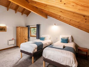 A bedroom with two beds, wooden beams, a window, and a wardrobe.