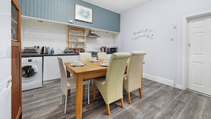A compact kitchen with a wooden dining table, white chairs, and a built-in oven. - Regency by the Sea @ Blackpool (Blackpool)
