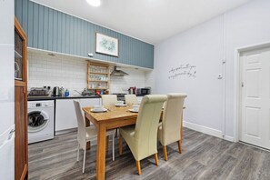 A compact kitchen with a wooden dining table, white chairs, and a built-in oven. - Regency by the Sea @ Blackpool (Blackpool)