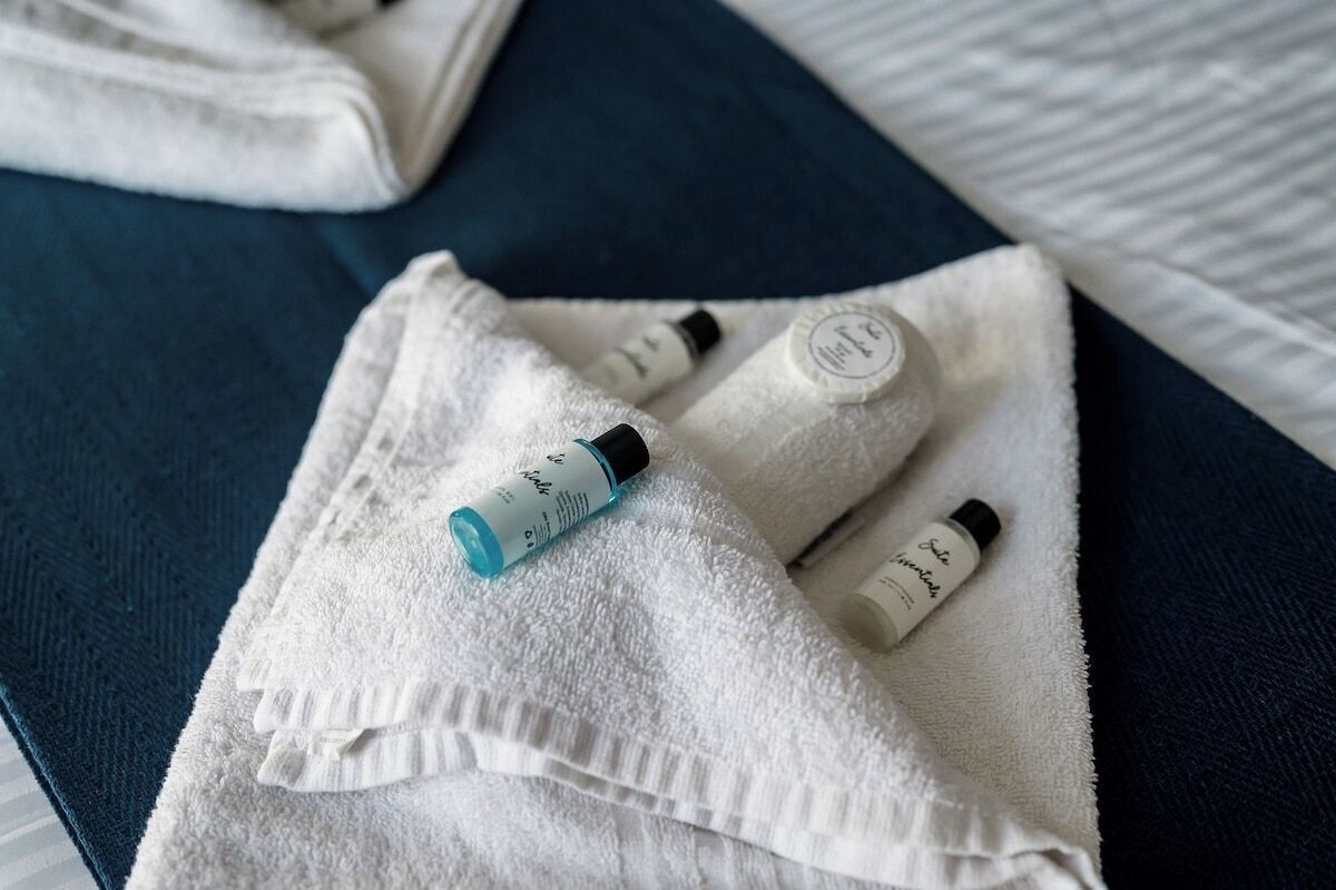 Una toalla blanca doblada con dos botellas de loción y un pequeño tubo sobre una superficie azul oscuro.