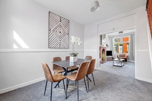 A modern dining area with a dark wooden table and six brown chairs, a decorative wall piece, and a potted plant. - StayMinorca @ Bolton (Bolton)