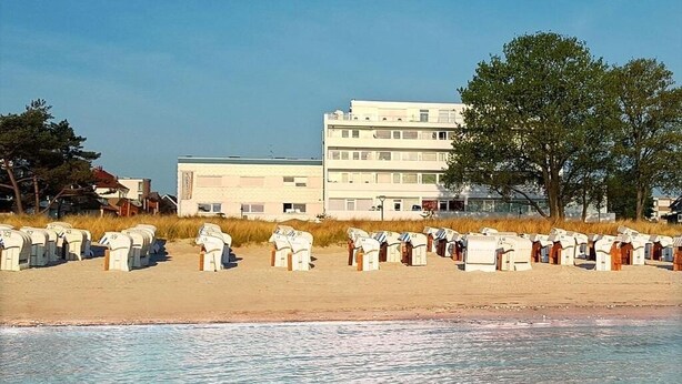 A beachside hotel with rows of beach chairs and a building with multiple floors. - Beachfront studio in Scharbeutz - comfort & tranquillity right by the sea (Scharbeutz)