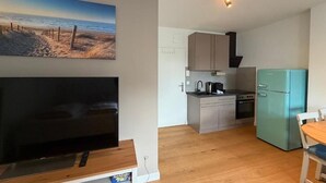 A compact kitchen with a TV, a teal refrigerator, and a dining area with a wooden table and chairs. - Beachfront studio in Scharbeutz - comfort & tranquillity right by the sea (Scharbeutz)