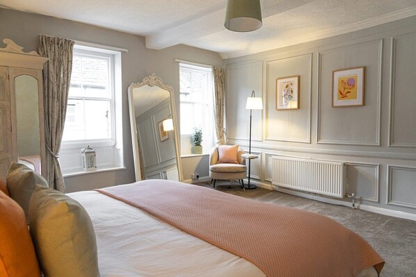 A hotel room with a large bed, a chair, a mirror, and framed artwork on the walls.
