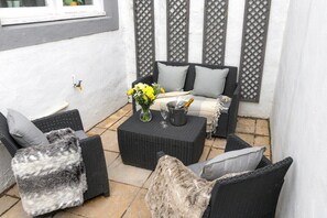 An outdoor seating area with wicker furniture, a table with a vase of flowers, and a bottle of champagne.