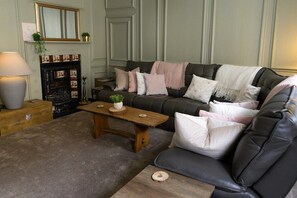 A cozy living room with a fireplace, a dark leather sofa, a wooden coffee table, and a lamp.
