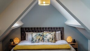 Ein Schlafzimmer mit einem gepolsterten Kopfteil, einem Bett mit weißer Bettwäsche, zwei Zierkissen, einer gelben Tagesdecke und zwei Nachttischlampen.
