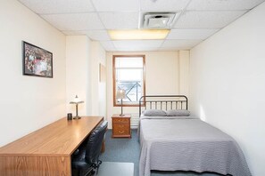 Ein kleines, ordentlich eingerichtetes Schlafzimmer mit Bett, Schreibtisch, Stuhl und Nachttisch.