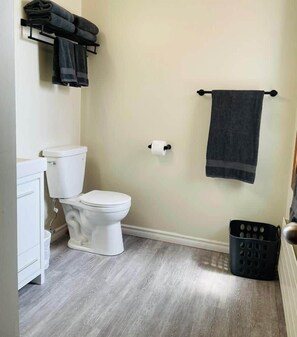 Ein Badezimmer mit Toilette, Waschbecken, Handtuchhalter mit Handtüchern und einem Mülleimer.
