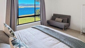 Un dormitori amb llit, sofà, finestra amb vista al mar i cortines.