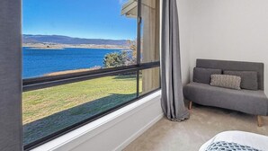 Habitació amb vista a una massa d'aigua, un sofà gris amb coixins i una finestra amb cortines.